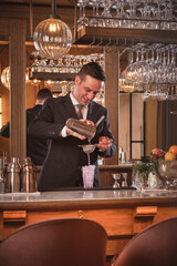 Bartender pouring cocktail through strainer in glass at counter