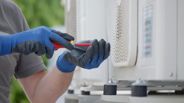 Professional HVAC technician performing maintenance on air conditioners, working with a screwdriver.