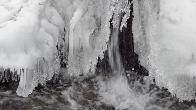This is a close up of water flowing under a cover of ice into a stream in winter.