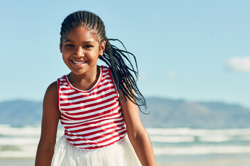 Portrait, smile and wind with black girl on beach in summer for holiday, travel or vacation. Breeze, coast and relax with happy African child outdoor by ocean or sea for tropical island getaway