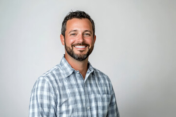 Obraz premium Smiling man in a casual plaid shirt standing against a plain grey background, exuding friendliness and approachability.