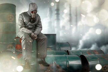 A man in a gas mask and protective suit sitting on a barrel of chemical waste with a chemical and...