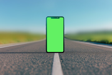 Creative photo. Close-up mobile phone standing in the middle of a highway road against a background of blue sky with clouds
