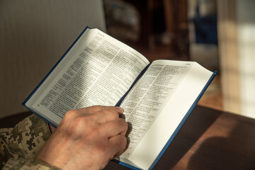 Fototapeta premium Hands of soldier in uniform holding the Holy Bible. Natural aesthetic light