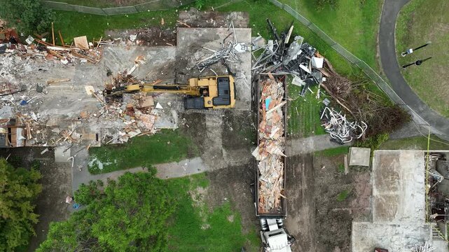 Drone top down static of building demolition as crane claw lifts to spin and drop broken wall rubble into back of truck