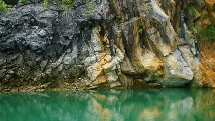An image of a rocky cliff face reflected in the calm, emerald-green waters of a lake.