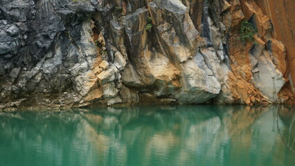 An image of a rocky cliff face reflected in the calm, emerald-green waters of a lake.
