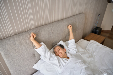 Beautiful woman waking up, stretching hands after good night sleep in hotel