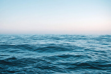 Obraz premium A Serene Morning by the Ocean: Gentle Waves Caress the Horizon Under a Clear Blue Sky with Hints of Warmth from Rising Sun