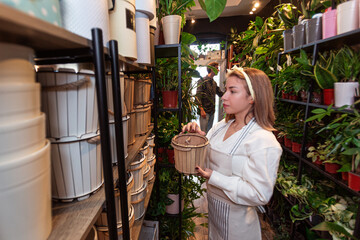 Female worker in the flower shop stacking shelf while a customer looks around the shop