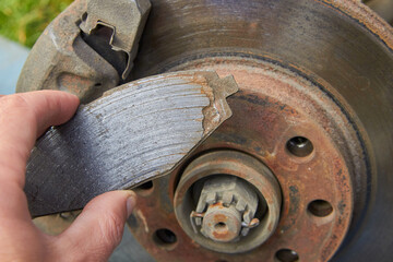 worn brake pad in hands, worn old brake pad on the background of the car disk