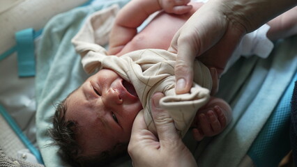 Mother helping newborn baby get dressed, delicate touch on infant's hand, showing care and attention, early moments of bonding and nurturing, tenderness and love in daily routine