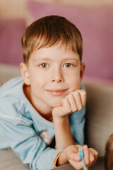 Cute 10 year old boy lies on his stomach on the sofa and looks at the camera