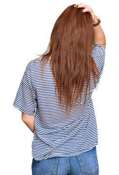 Young read head woman wearing casual clothes and glasses backwards thinking about doubt with hand on head