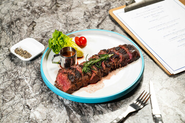 grilled Beef belly steak slice with butter, lettuce, cherry tomato, dip, fork and knife served in plate isolated on marble background side view of hong kong food