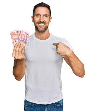 Handsome man with beard holding south african 50 rand banknotes pointing finger to one self smiling happy and proud