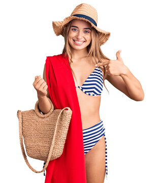 Young beautiful blonde woman wearing bikini and hat holding summer wicker handbag pointing finger to one self smiling happy and proud