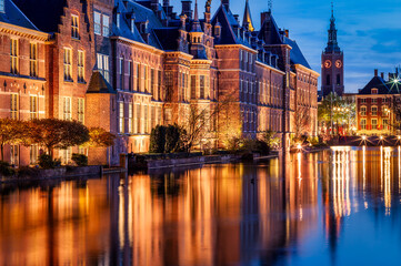 Senate building of the Dutch parliament complex illuminated at dusk in The Hague, The Netherlands. In the back, Grote Kerk tower clock indicates 9:35pm