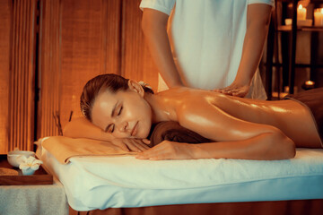 Obraz premium Caucasian woman customer enjoying relaxing anti-stress spa massage and pampering with beauty skin recreation leisure in warm candle lighting ambient salon spa at luxury resort or hotel. Quiescent