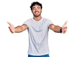 Hispanic young man with beard wearing casual white t shirt looking at the camera smiling with open arms for hug. cheerful expression embracing happiness.