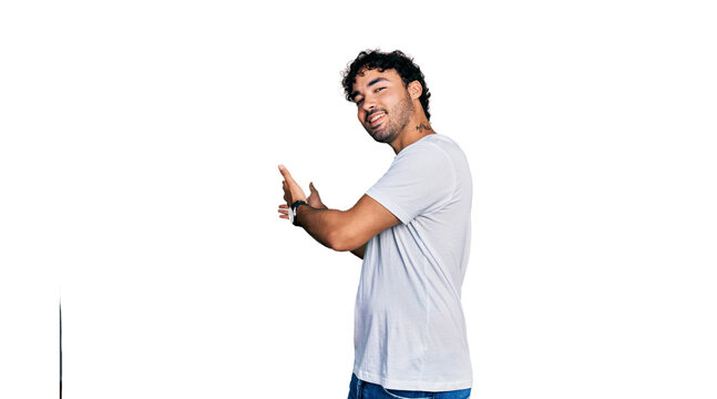 Hispanic young man with beard wearing casual white t shirt inviting to enter smiling natural with open hand