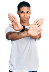 Young hispanic man wearing casual white t shirt rejection expression crossing arms doing negative...