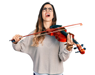 Beautiful hispanic woman playing violin angry and mad screaming frustrated and furious, shouting with anger looking up. © Krakenimages.com