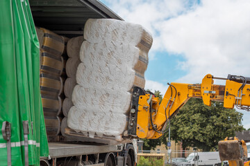 Loading Bales of Material Onto Truck Using Crane in Sunny Outdoor Setting