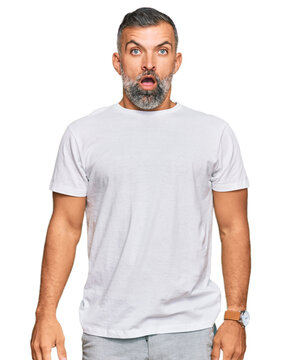 Middle age handsome man wearing casual white tshirt in shock face, looking skeptical and sarcastic, surprised with open mouth