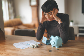 Woman Stressed Over Bills and Finances at Home, Sitting by a Piggy Bank and Cash on the Table