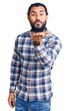Young arab man wearing casual clothes looking at the camera blowing a kiss with hand on air being lovely and sexy. love expression.