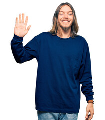 Handsome caucasian man with long hair wearing casual winter sweater waiving saying hello happy and smiling, friendly welcome gesture