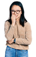 Young chinese woman wearing casual sweater and glasses looking stressed and nervous with hands on mouth biting nails. anxiety problem.