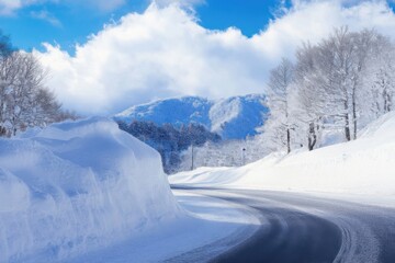 Obraz premium A snowy mountain road winding through a winter landscape with blue sky and white clouds.