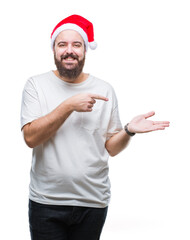 Young caucasian hipster man wearing christmas hat over isolated background amazed and smiling to the camera while presenting with hand and pointing with finger.