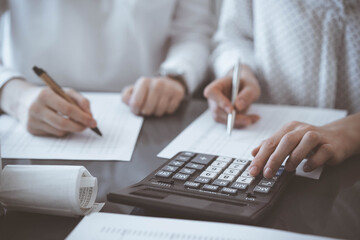 Two accountants use a calculator and laptop computer for counting taxes or revenue balance. Business, audit, and taxes concepts