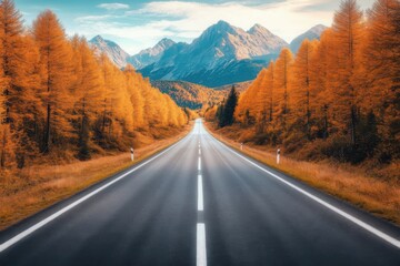 Fototapeta premium A serene road leading through picturesque autumn trees toward majestic mountains under a blue sky.