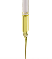 A drop of liquid yellow oil serum in a pipette on a gray background. Peeling, aha acid, collagen skin care liquid, close-up photo with shallow depth of field.