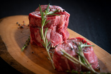 Raw Filet Mignon on a cutting board with rosemary and black pepper.
