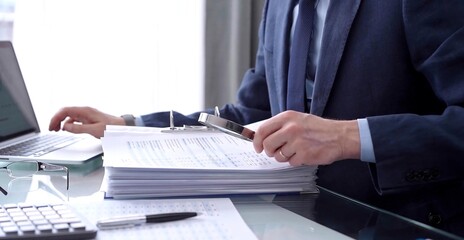 Businessman or auditor is looking through binders with papers while using a calculator and magnifying glass for financial documents analyzing. Audit and taxes concept