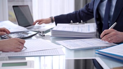 Business people wearing blue suits are reviewing financial data in office. Two professionals analyzing paper reports using calculators. Audit and taxes concept