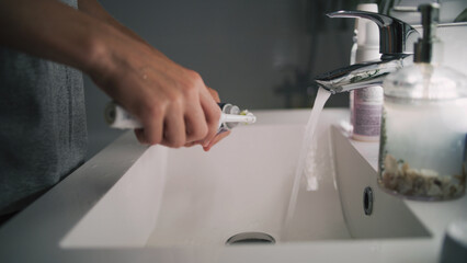 Caucasian boy looks at mirror in bathroom, brushes his teeth. Teenager stands in front of sink and uses electrical toothbrush before bedtime. Evening bath routine. Lifestyle concept. Low angle shot.