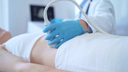 Doctor man wearing a blue medical gloves using an ultrasound equipment on a female patient lying down in clinic cabinet, close up view. Medicine concept