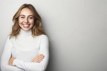 Fototapeta premium Attractive, cheerful young woman in a white turtleneck, smiling with arms crossed against an isolated background, creating space for additional content or text.