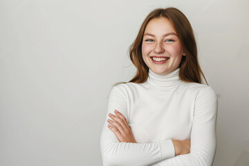 Fototapeta premium Attractive, cheerful young woman in a white turtleneck, smiling with arms crossed against an isolated background, creating space for additional content or text.