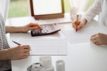 Two accountants using a calculator and laptop computer for counting taxes at white desk in office....