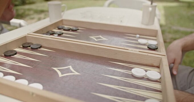 Close-up of a backgammon game in progress. Players are moving black and white pieces on a wooden board during the game play.