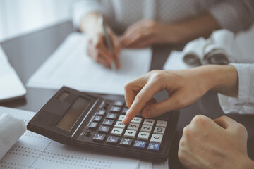 Woman accountant using a calculator and laptop computer while counting taxes for a client. Business audit and finance concepts
