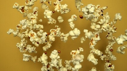 Slow motion shot of popcorn was throwing with yellow background. Fresh movie popcorn moving and falling. Popcorn in motion falling in a captivating dance. Dynamic movement and energy. Comestible.