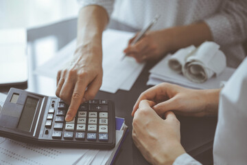 Woman accountant using a calculator and laptop computer while counting taxes for a client. Business...